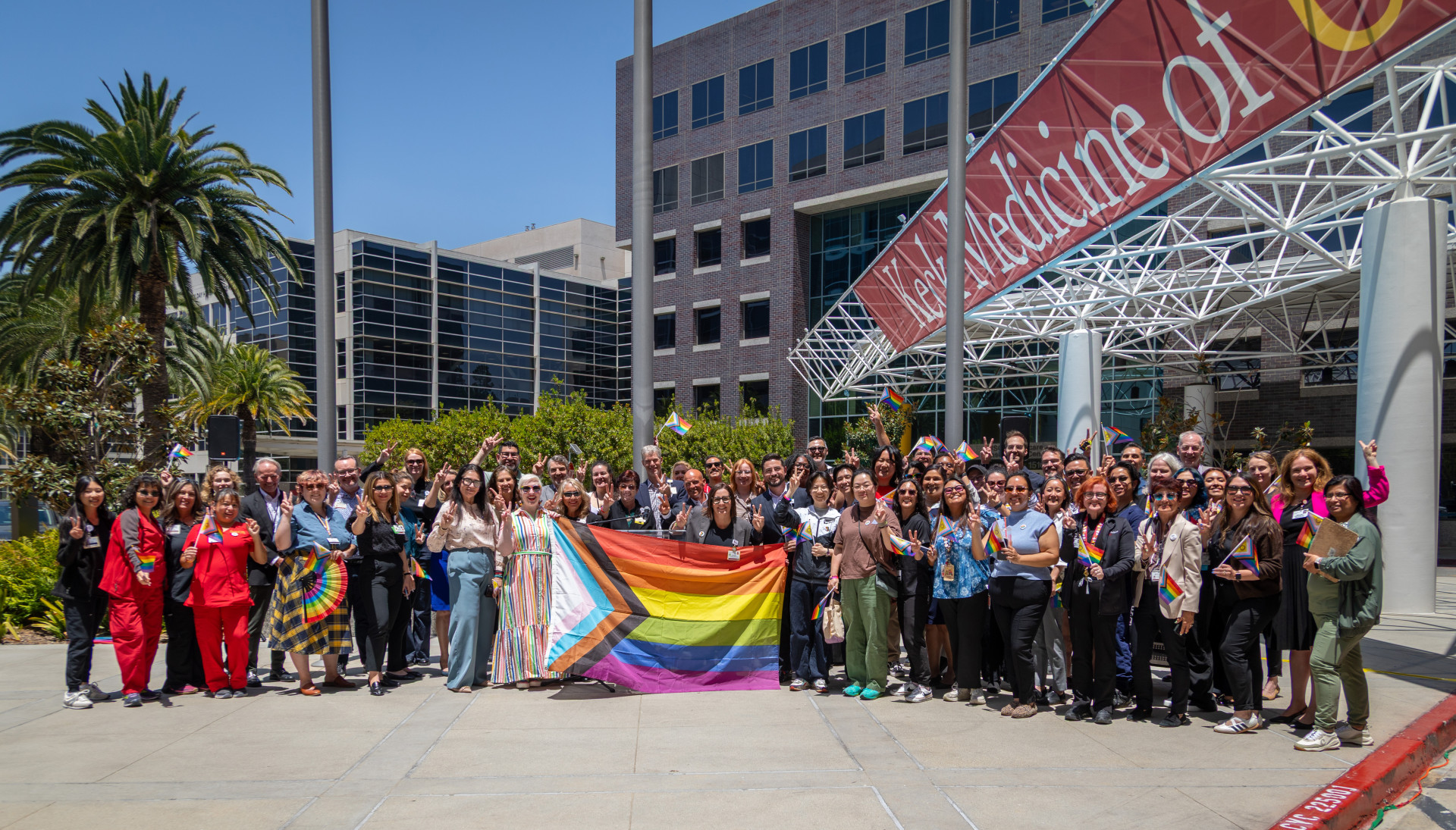 a large group of people standing outside a USC Keck building holding a rainbow Pride flag